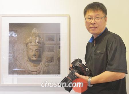 
	오세윤씨가‘석굴암 십일면 관음보살’을 찍은 사진 앞에서 카메라를 들고 서있다.
